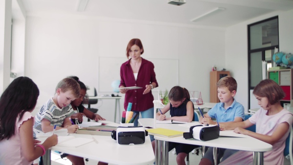 A group of small school kids with VR goggles and teacher in class, learning.