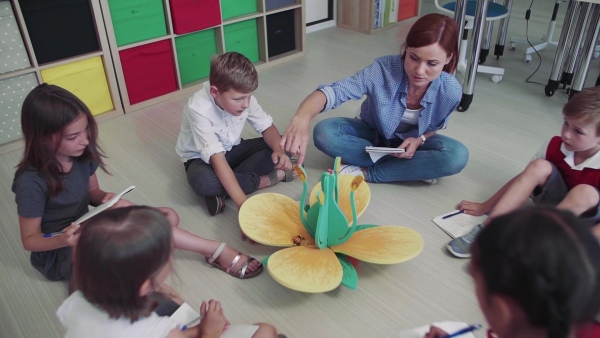 A group of small school kids with teacher sitting on the floor in class, learning science. Slow motion.