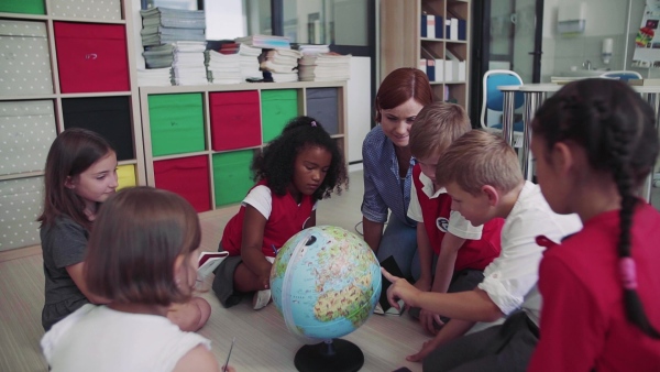 A group of small school kids with teacher sitting on the floor in class, learning geography. Slow motion.