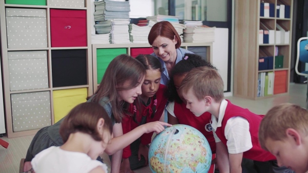 A group of small school kids with teacher sitting on the floor in class, learning geography. Slow motion.