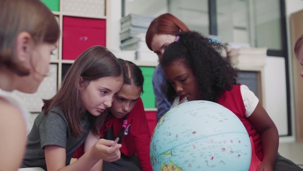 A group of small school kids with teacher sitting on the floor in class, learning geography. Slow motion.