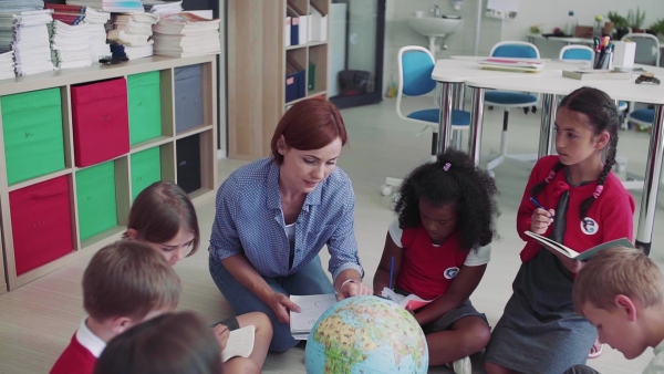 A group of small school kids with teacher sitting on the floor in class, learning geography. Slow motion.