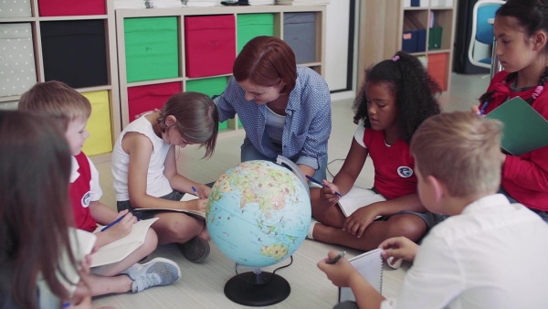 A group of small school kids with teacher sitting on the floor in class, learning geography. Slow motion.