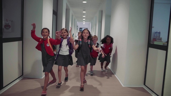 A group of cheerful small school kids in corridor, running. Back to school concept. Slow motion.