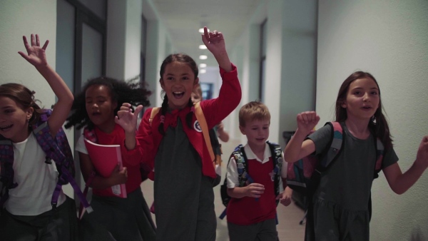 A group of cheerful small school kids in corridor, running. Back to school concept. Slow motion.