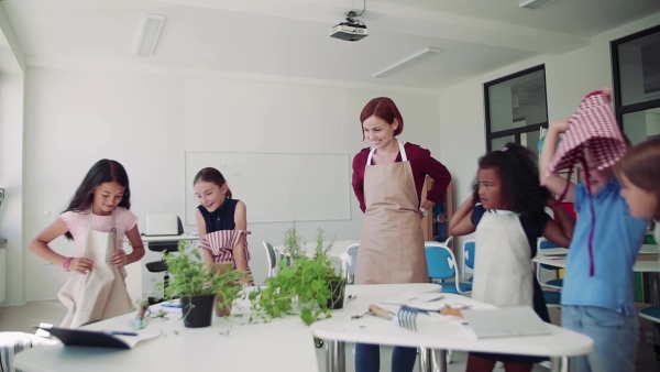 A group of small school kids with teacher standing around table in class, planting herbs.