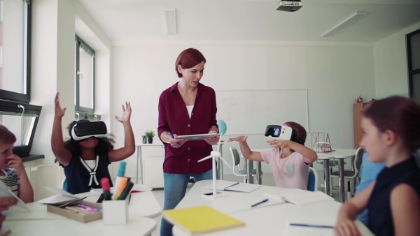 A group of small school kids with VR goggles and teacher in class, learning. Slow motion.