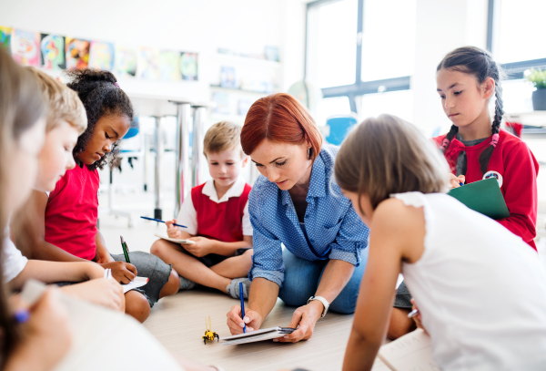 A group of small school kids with teacher sitting on the floor in class, learning science.