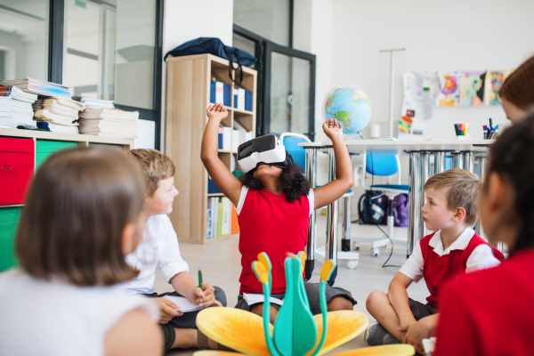 A group of small school kids with VR goggles sitting on the floor in class, learning science.