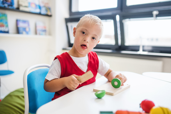 A happy down-syndrome school boy sitting at the desk in the classroom, learning.