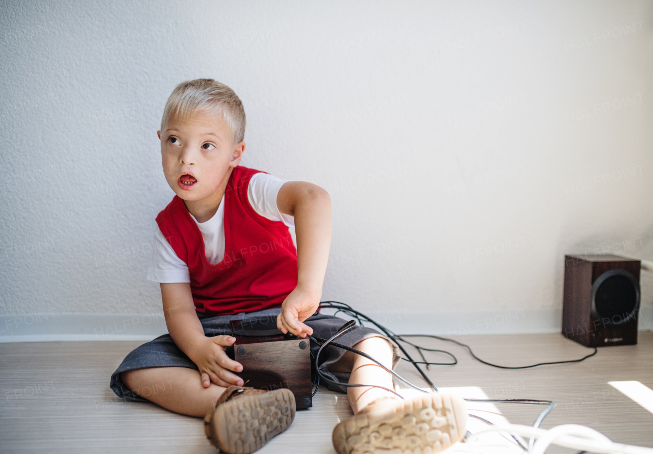 A portrait of happy down-syndrome school boy sitting on the floor, playing with loudspeakers.