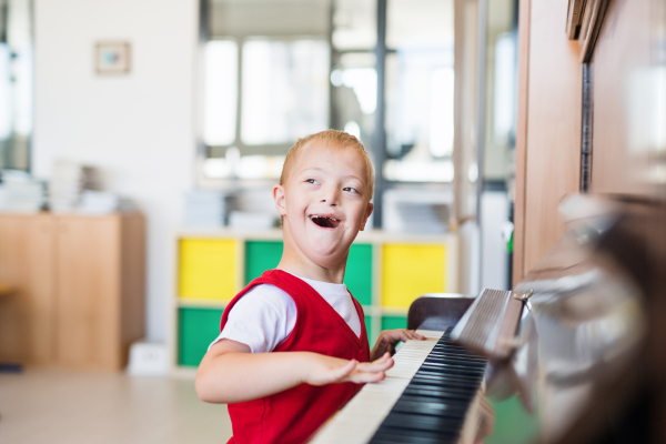 A cheerful down-syndrome school boy sitting at school, playing piano.