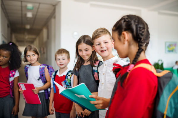 A group of cheerful small school kids with bags standing in corridor, talking. Back to school concept.