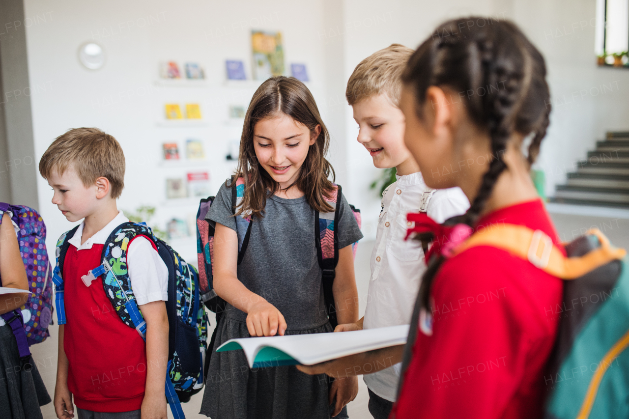 A group of cheerful small school kids with bags walking in corridor, talking. Back to school concept.