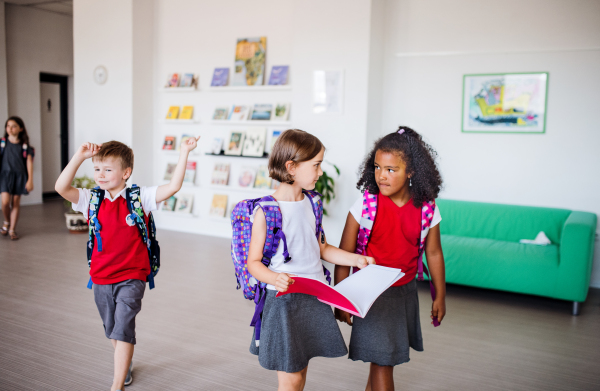 A group of cheerful small school kids with bags walking in corridor. Back to school concept.