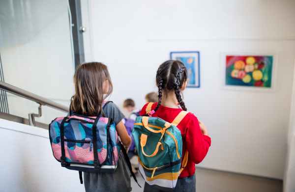 Rear view of small school girl friends with bags walking down the stairs. Back to school concept.