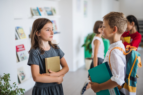 A group of cheerful small school kids with bags walking in corridor, talking. Back to school concept.