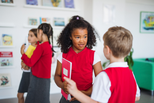 A group of cheerful small school kids in corridor, standing and talking. Back to school concept.