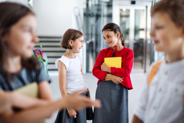 A group of cheerful small school kids in corridor, standing and talking. Back to school concept.