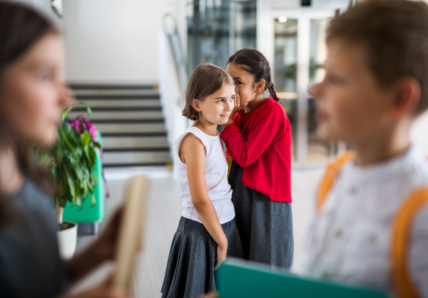 A group of cheerful small school kids in corridor, standing and talking. Back to school concept.