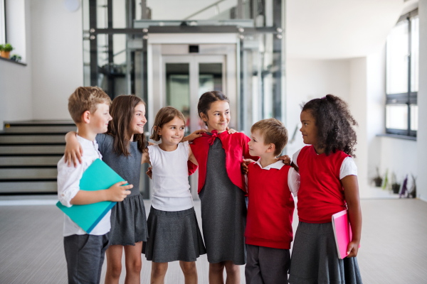 A group of cheerful small school kids standing in corridor. Back to school concept.