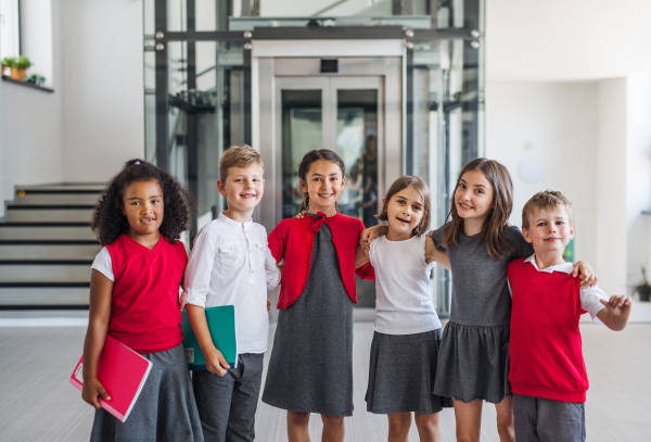 A group of cheerful small school kids in corridor, looking at camera. Back to school concept.