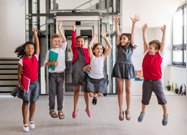 A group of cheerful small school kids in corridor, jumping. Back to school concept.