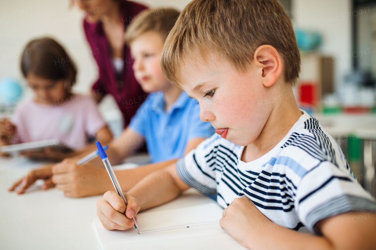 A group of small school kids with teacher sitting at the desk in class writing.