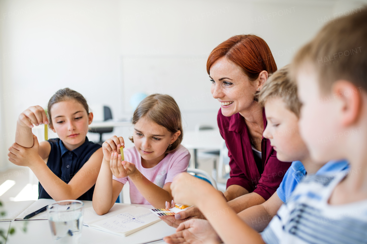 A group of small school kids with teacher sitting on the floor in class, learning science.