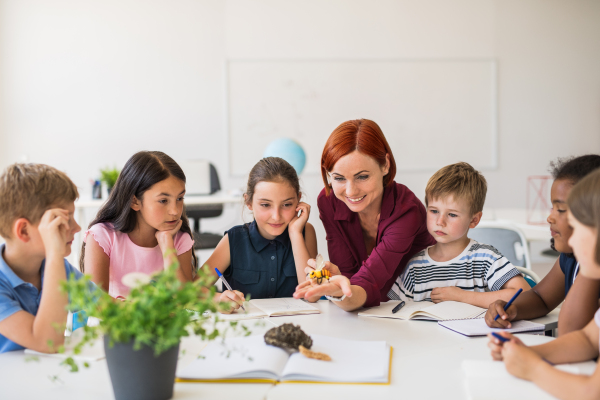 A group of small school kids with teacher sitting at desk in circle in class, learning science.