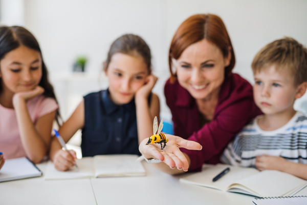 A group of small school kids with teacher sitting at desk in circle in class, learning science.