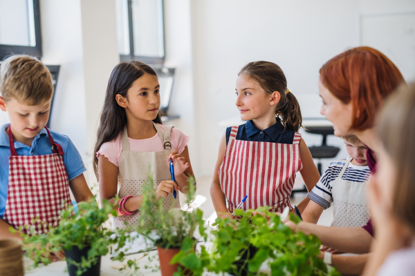 A group of small happy school kids with teacher standing in circle in class, planting herbs.