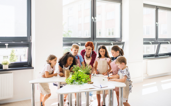 A group of small happy school kids with teacher standing in circle in class, planting herbs.