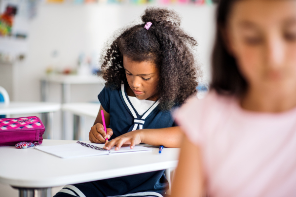 A small mixed race happy school girl sitting at the desk in classroom, writing.