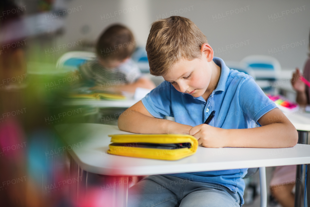 A small happy school boy sitting at the desk in classroom, writing notes.