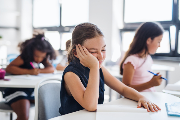 A small tired and bored school girl sitting at the desk in classroom, sleeping.