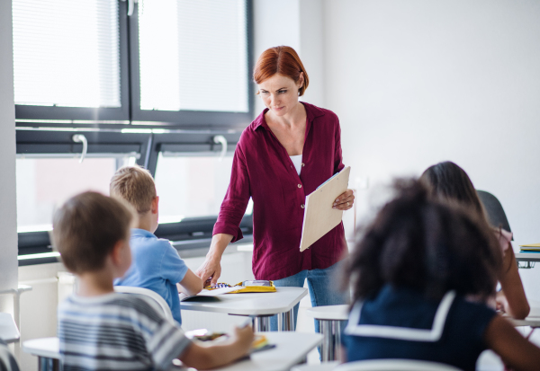 A friendly teacher walking among small school children on the lesson, explaining and helping.