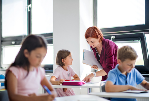 A friendly teacher walking among small school children on the lesson, explaining and helping.