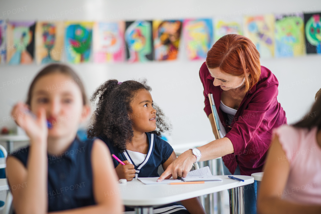 A friendly teacher walking among small school children on the lesson, explaining and helping.