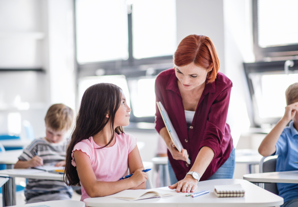 A friendly teacher walking among small school children on the lesson, explaining and helping.