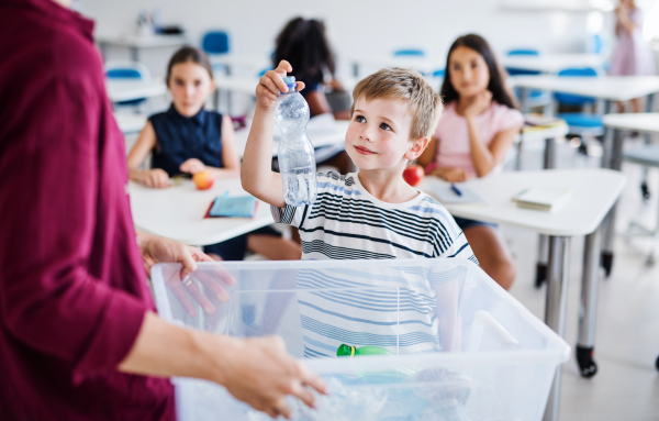 An unrecognizable teacher with small school kids in classroom learning about ecological waste separation.