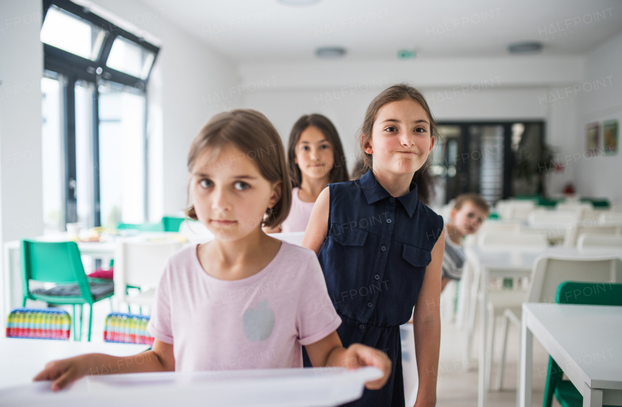 A group of cheerful small school kids with plastic trays in canteen, walking.