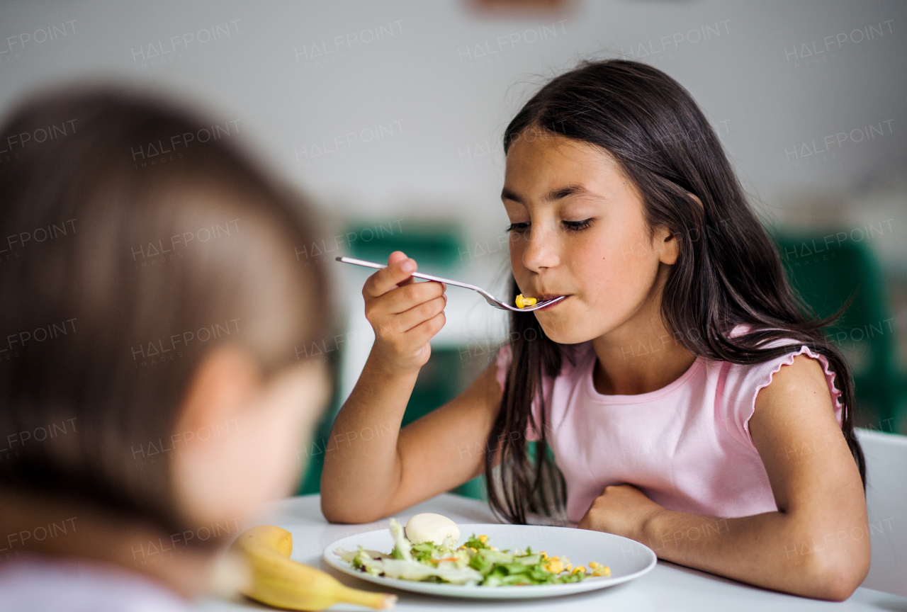 Two small school girlas in canteen, eating lunch.