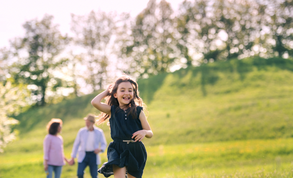 A small girl with grandparents in the background on a walk outside in spring nature.