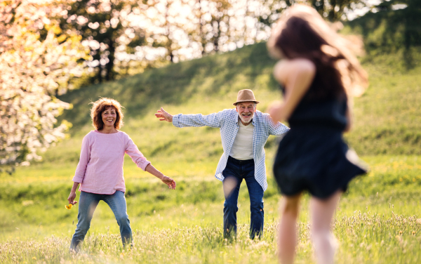 An unrecognizable small girl with grandparents in the background running outside in spring nature.