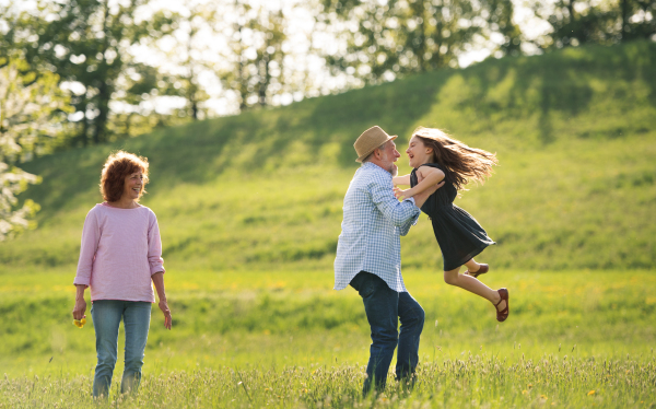 Happy senior couple with granddaughter outside in spring nature, having fun.