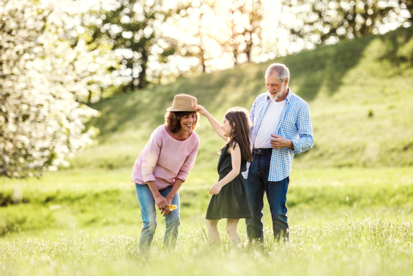 Happy senior couple with granddaughter outside in spring nature, having fun.