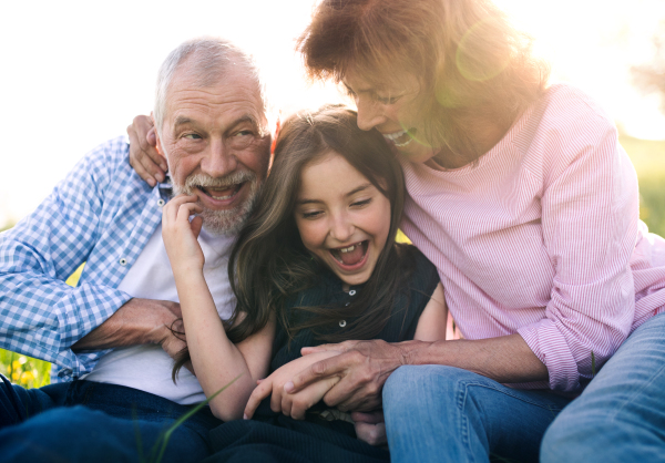 Senior couple with granddaughter outside in spring nature, relaxing on the grass and having fun.