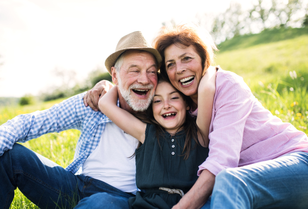 Senior couple with granddaughter outside in spring nature, relaxing on the grass and having fun.