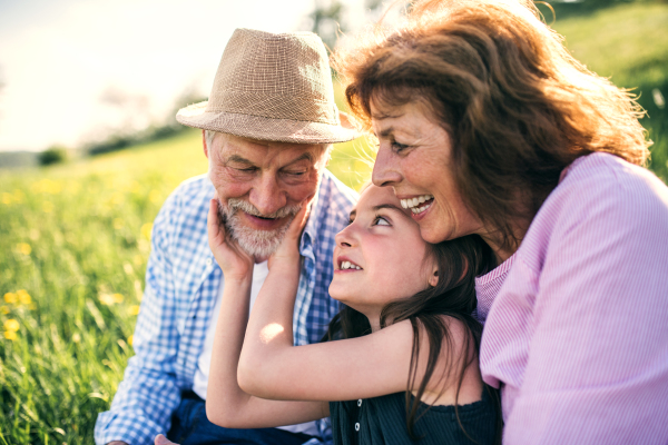 Senior couple with granddaughter outside in spring nature, relaxing on the grass and having fun. Close up.